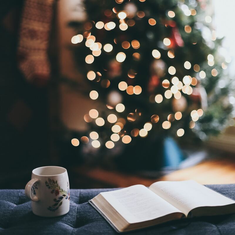 Boek met kop koffie en kerstboom met lampjes op achtergrond